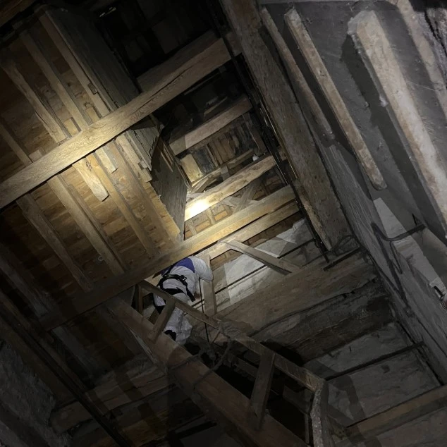 Photo d'un technicien spécialisé en dépigeonnage en hauteur dans une église réalisant un nettoyage des fientes et la pose de dispositifs anti pigeon.