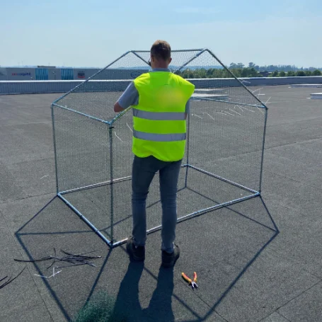 Photo d'un technicien réalisant la pose d'une cage pigeon sur un toit d'un entrepôt logistique dans les Hauts-de-France.